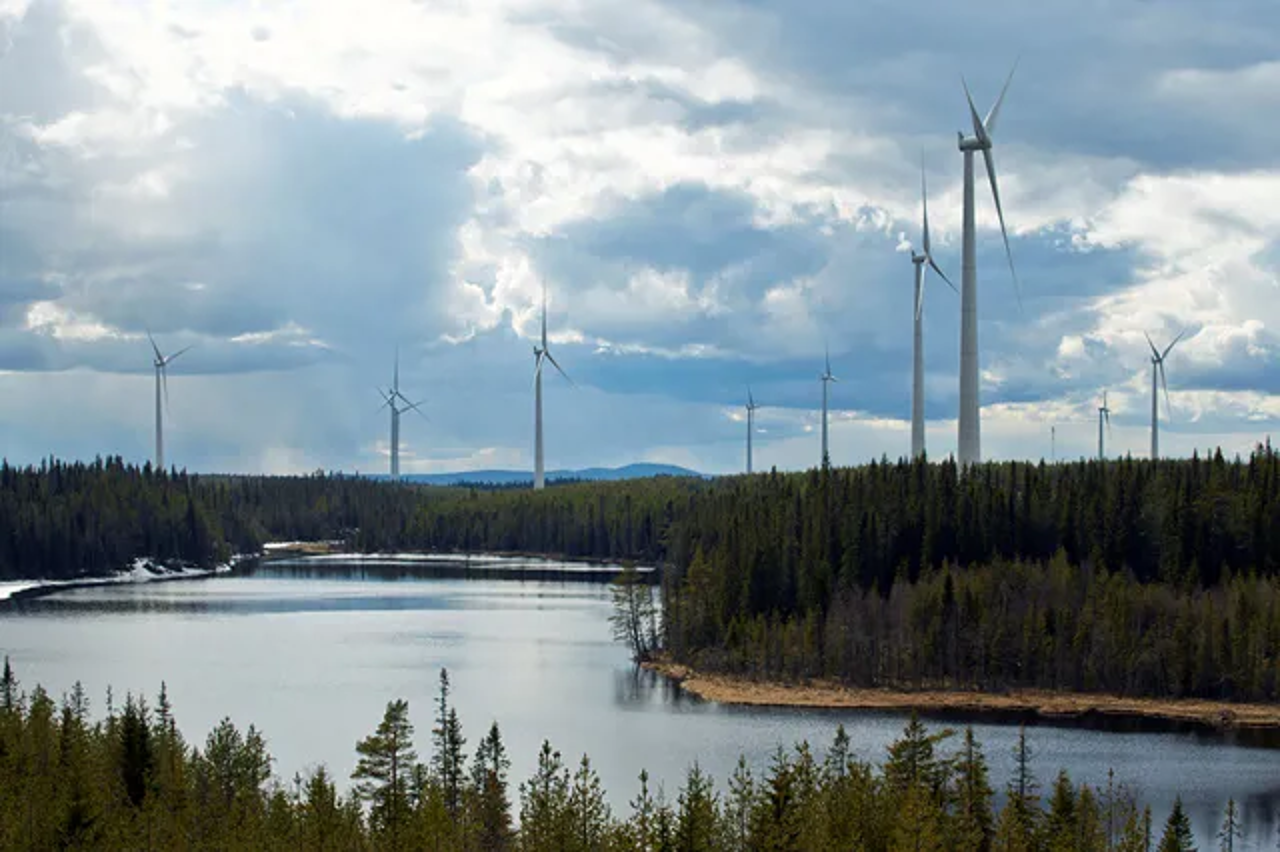 En vid bild över Mörttjänbergets vindkraftpark där ett antal vindkraftverk är synliga mot molnig himmel. 