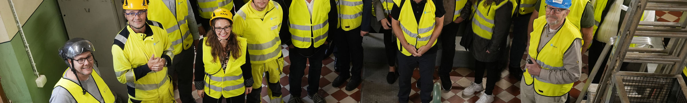 En grupp människor i varselkläder bredvid vattenkraftsturbiner