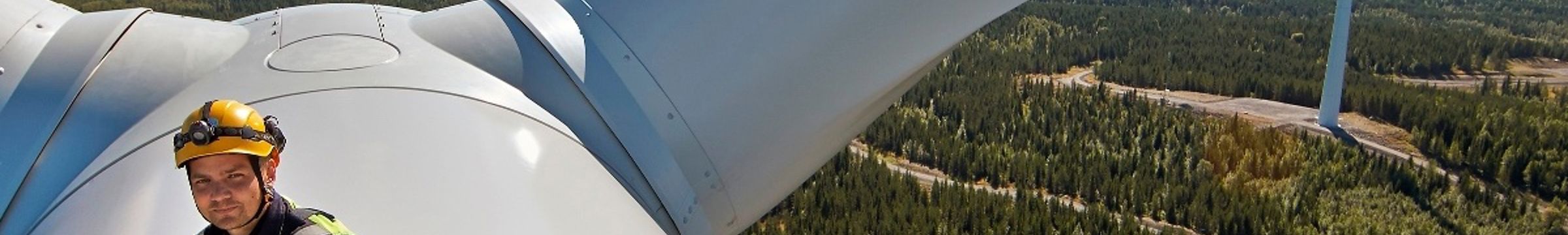En man i varselkläder på toppen av en vindkraftsturbin